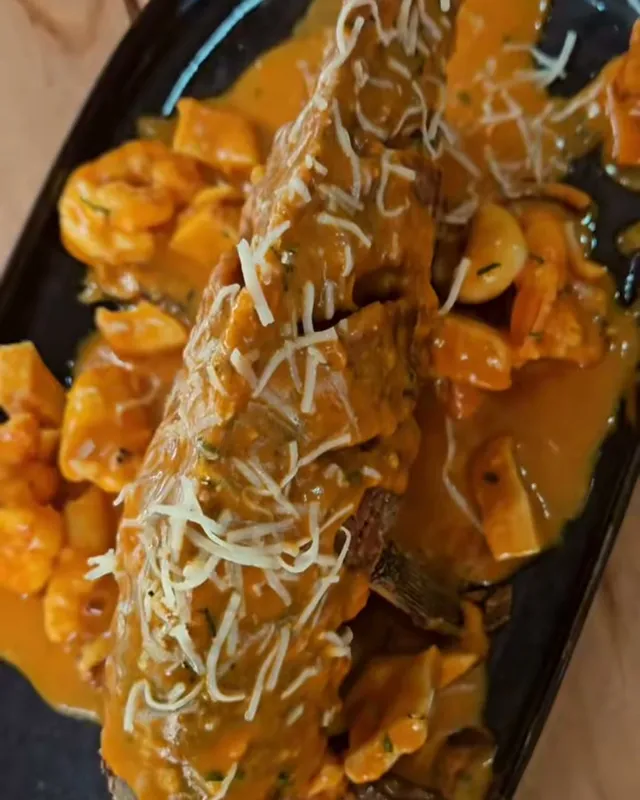 Un pescado entero frito, bañado en salsa de mariscos con queso